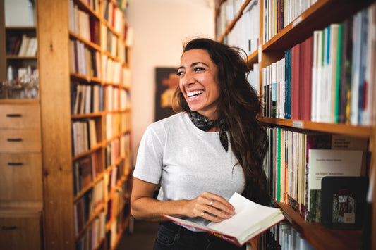 Smiling person in a library, holding a book